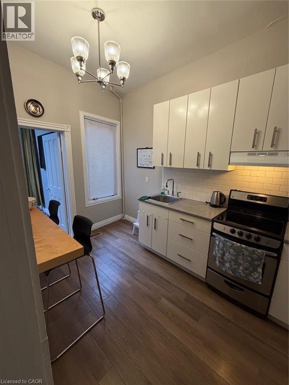 Kitchen with stove, dark wood-style flooring, a chandelier, white cabinetry, and pendant lighting - 175 John Street S, Hamilton, ON