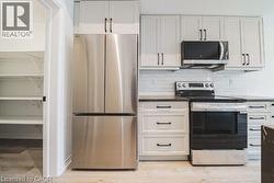 Kitchen with stainless steel appliances, white cabinetry, decorative backsplash, and light wood finished floors -