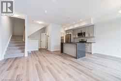 Kitchen with gray cabinets, open floor plan, a center island with sink, dark countertops, and light wood-style flooring -