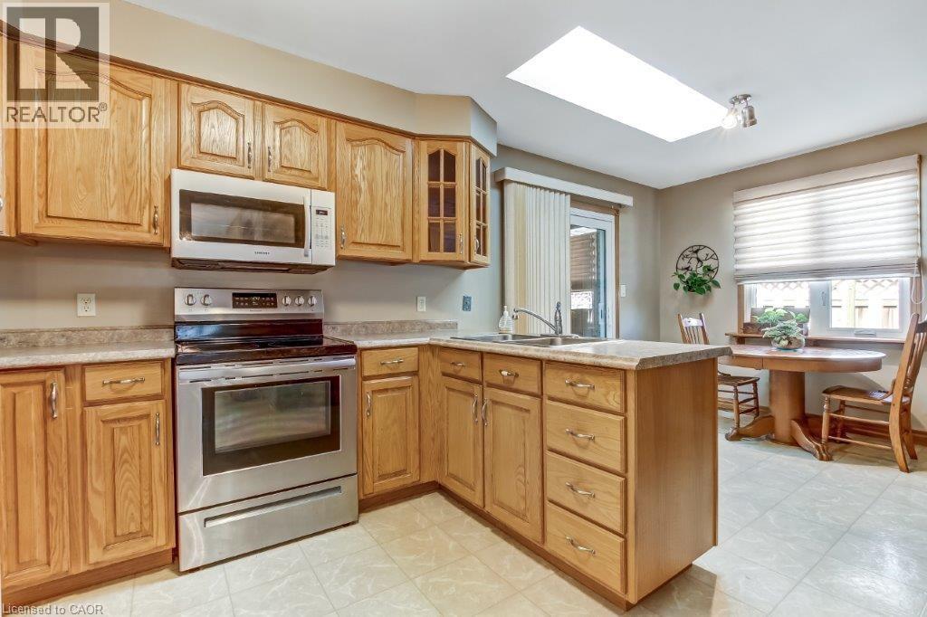 Kitchen with stainless steel electric stove, a skylight, glass insert cabinets, white microwave, and light countertops - 2 Falls Crescent, Simcoe, ON - Indoor Photo Showing Kitchen With Double Sink