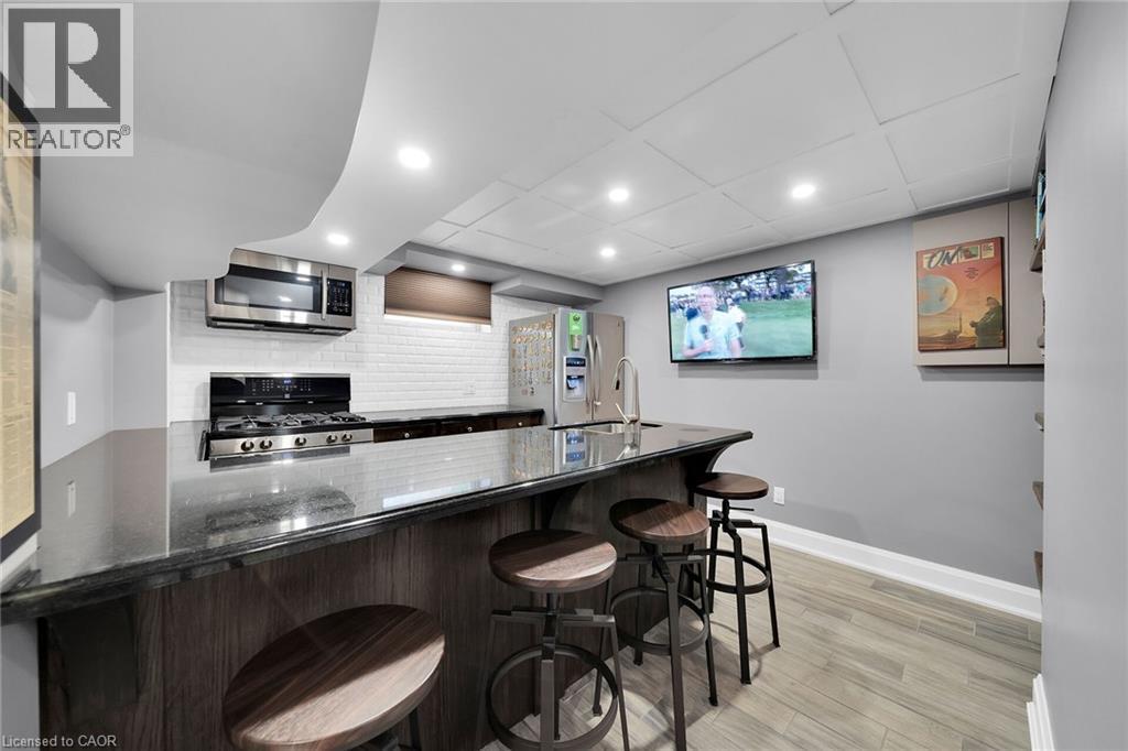 Kitchen featuring backsplash, appliances with stainless steel finishes, a kitchen bar, light wood-type flooring, and a peninsula - 404 Mountain Brow Boulevard E, Hamilton, ON - Indoor
