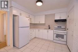Kitchen featuring white cabinetry, white appliances, light countertops, and under cabinet range hood -