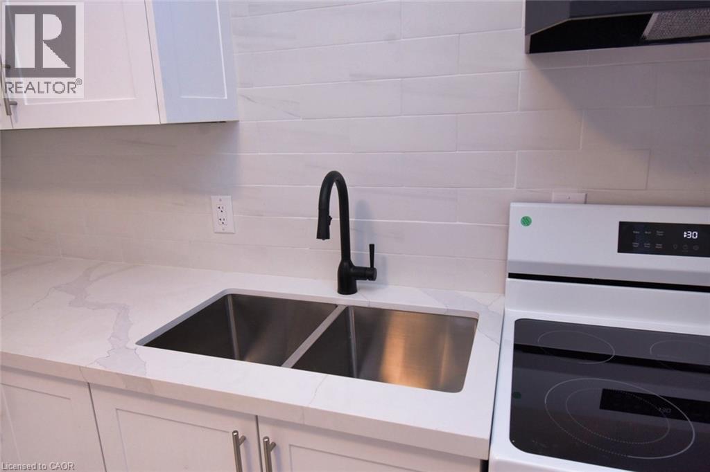 Kitchen view of white cabinets, white range with electric cooktop, ventilation hood, light quartz counters, and decorative backsplash - 215 Walter Avenue S, Hamilton, ON - Indoor Photo Showing Kitchen With Double Sink