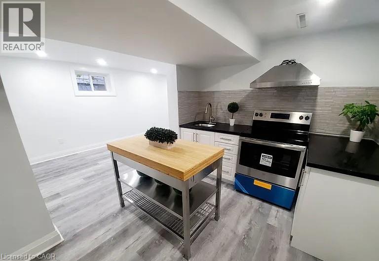 Kitchen featuring dark countertops, backsplash, stainless steel electric range, white cabinetry, and wall chimney range hood - 549 Waterloo Street, Hamilton, ON - Indoor