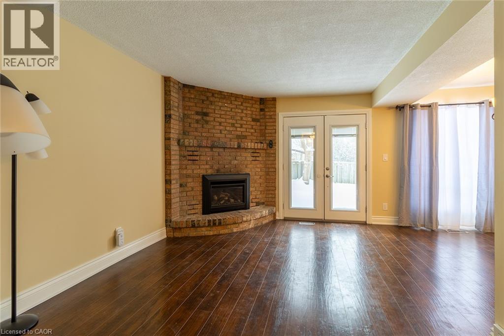 Unfurnished living room featuring french doors, a textured ceiling, dark wood finished floors, and a brick fireplace - 58 Romy Crescent, Thorold, ON - Indoor Photo Showing Living Room With Fireplace