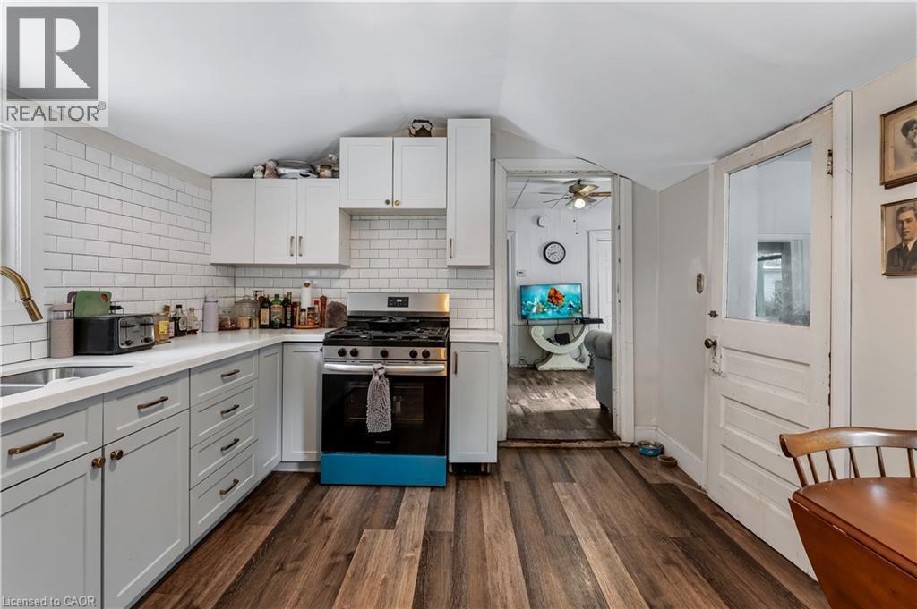 Kitchen with stainless steel gas range, decorative backsplash, dark wood-style floors, white cabinets, and lofted ceiling - 193 Locke Street N, Hamilton, ON - Indoor Photo Showing Kitchen With Double Sink
