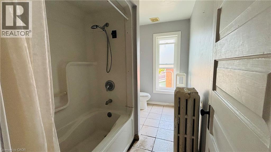 Bathroom featuring radiator, light tile patterned floors, and shower / washtub combination - 30 Regina Street N, Waterloo, ON - Indoor Photo Showing Bathroom