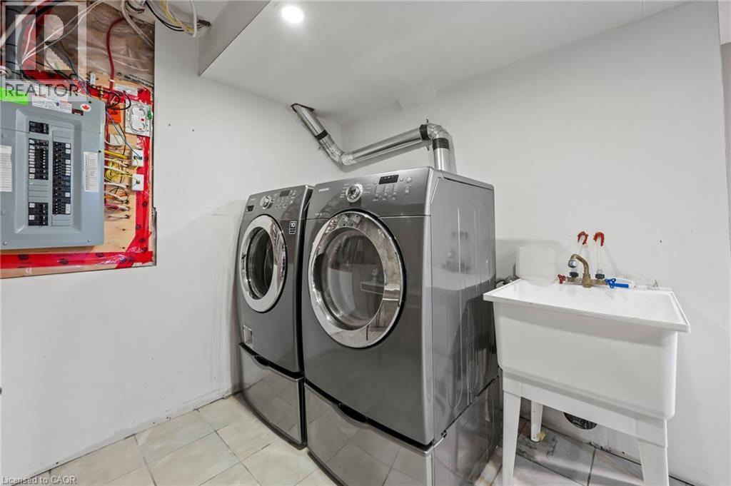Clothes washing area featuring washing machine and clothes dryer, electric panel, laundry area, tile patterned floors, and a sink - 561 Thomas Slee Drive, Kitchener, ON - Indoor Photo Showing Laundry Room
