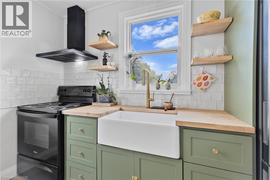 Kitchen featuring green cabinetry, black electric range, wall chimney exhaust hood, open shelves, and crown molding - 191 East 11Th Street, Hamilton, ON - Indoor Photo Showing Kitchen With Double Sink