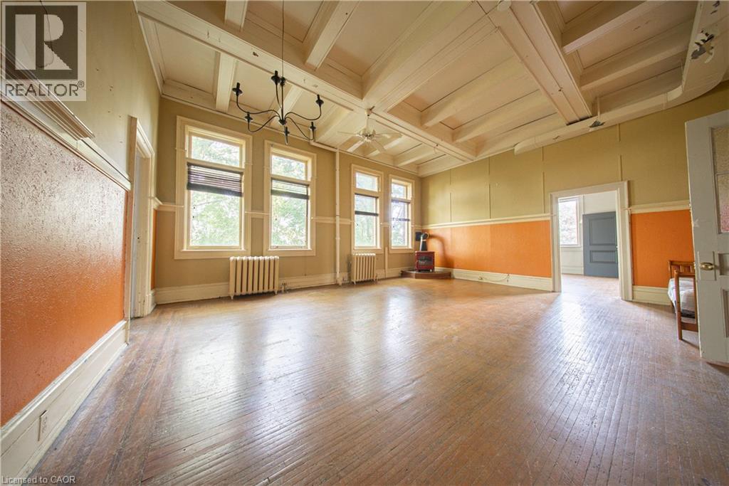 Unfurnished living room featuring hardwood / wood-style flooring, beam ceiling, plenty of natural light, wainscoting, and radiator - 231 Bay Street N, Hamilton, ON