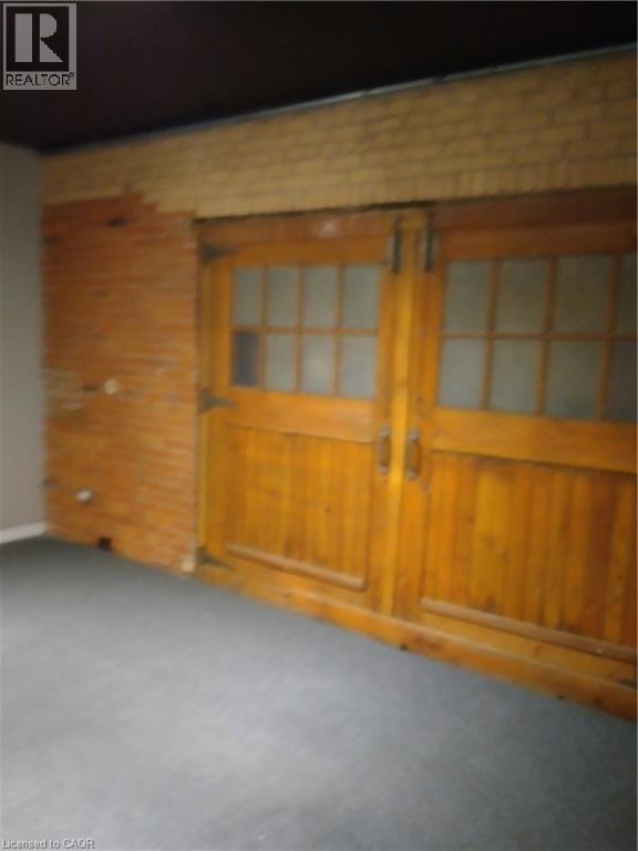 Empty room with brick wall, carpet floors, and wooden walls - 12 Ferguson Avenue N, Hamilton, ON