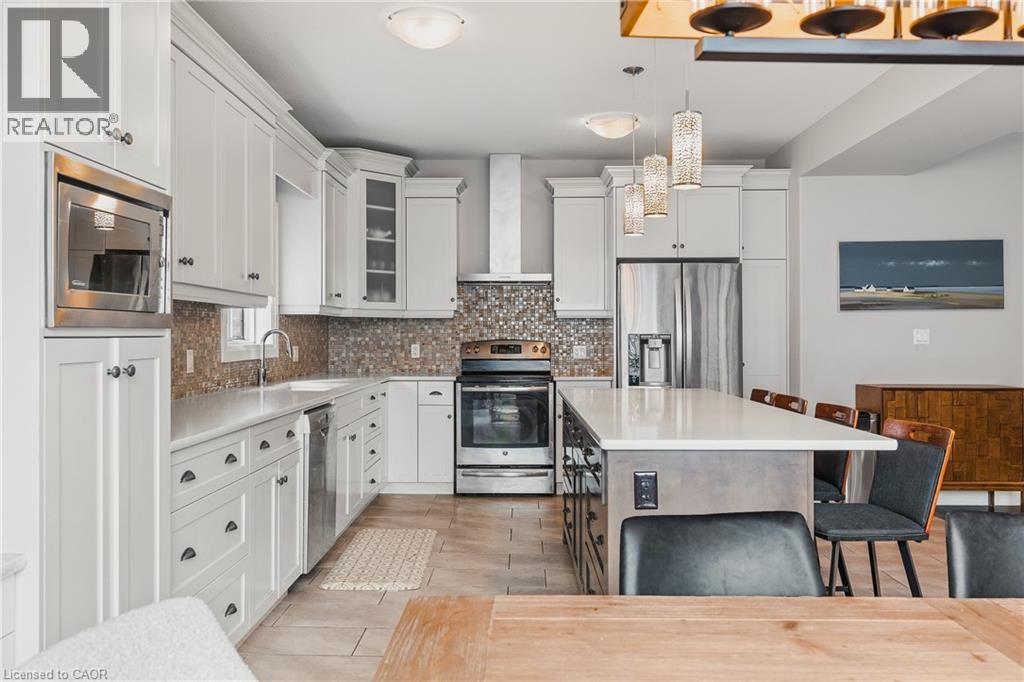 Kitchen featuring a breakfast bar area, appliances with stainless steel finishes, glass insert cabinets, wall chimney exhaust hood, and white cabinetry - 346 Moorlands Crescent, Kitchener, ON - Indoor Photo Showing Kitchen With Upgraded Kitchen