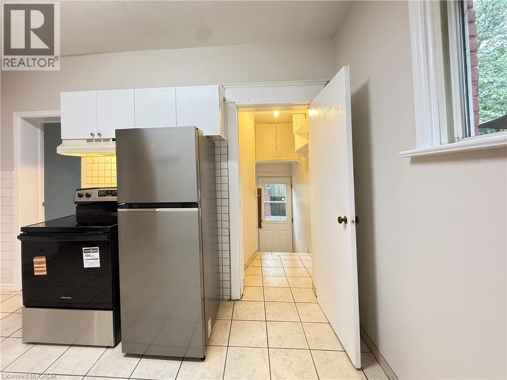 Kitchen with stainless steel appliances, under cabinet range hood, light tile patterned floors, and white cabinetry - 24 Somerset Avenue, Hamilton, ON - Indoor Photo Showing Kitchen