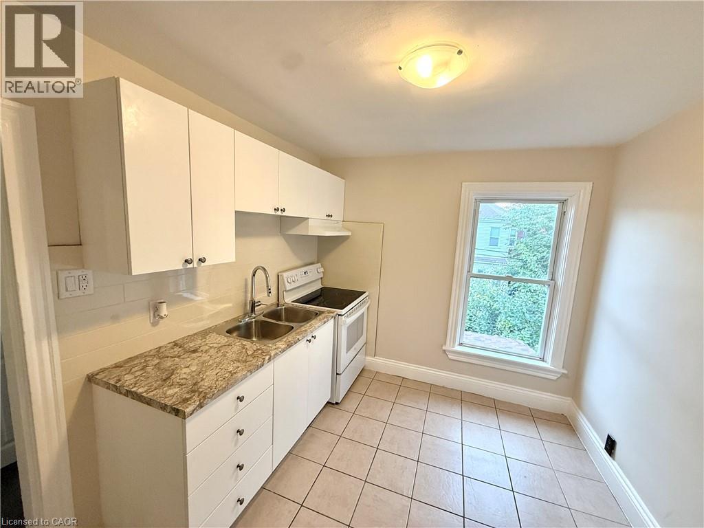 Kitchen with white electric range, white cabinetry, light tile patterned flooring, light countertops, and under cabinet range hood - 24 Somerset Avenue, Hamilton, ON - Indoor Photo Showing Kitchen With Double Sink