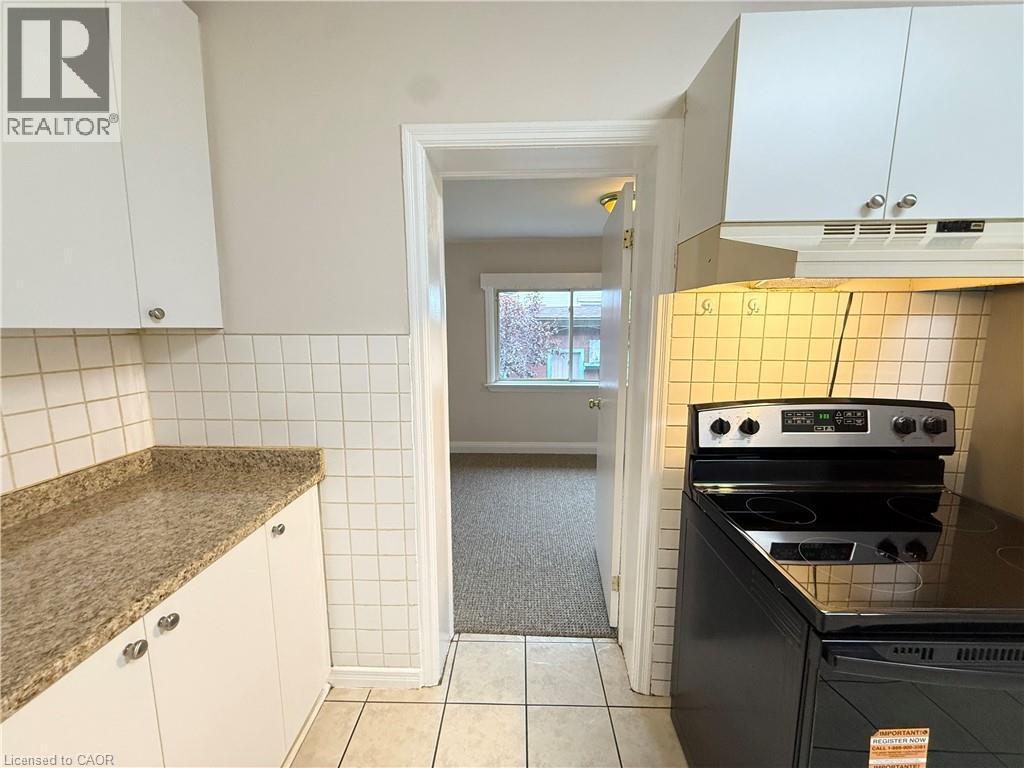 Kitchen featuring black range with electric cooktop, white cabinets, light tile patterned floors, tile walls, and under cabinet range hood - 24 Somerset Avenue, Hamilton, ON - Indoor Photo Showing Kitchen