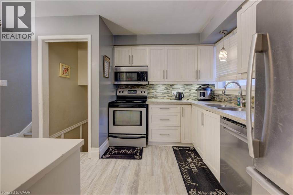 Kitchen with stainless steel appliances, decorative backsplash, light stone counters, light wood-style floors, and hanging light fixtures - 31 Bonfair Court, Kitchener, ON - Indoor Photo Showing Kitchen With Double Sink
