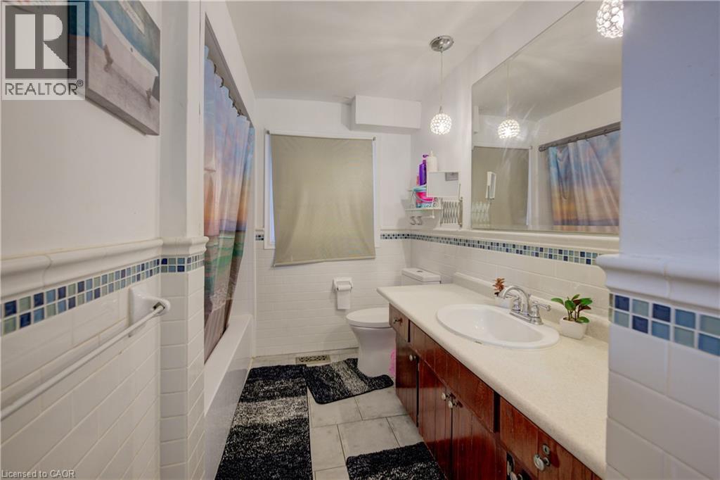 Full bathroom featuring light tile patterned floors, vanity, tile walls, shower / bath combination with curtain, and a wainscoted wall - 31 Bonfair Court, Kitchener, ON - Indoor Photo Showing Bathroom