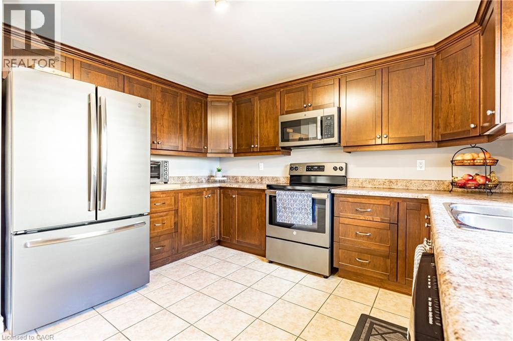 Kitchen with stainless steel appliances, brown cabinets, light tile patterned floors, and light stone countertops - 28 Springbreeze Heights, Hamilton, ON - Indoor Photo Showing Kitchen