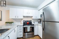 Kitchen with appliances with stainless steel finishes, white cabinetry, backsplash, under cabinet range hood, and a textured ceiling -