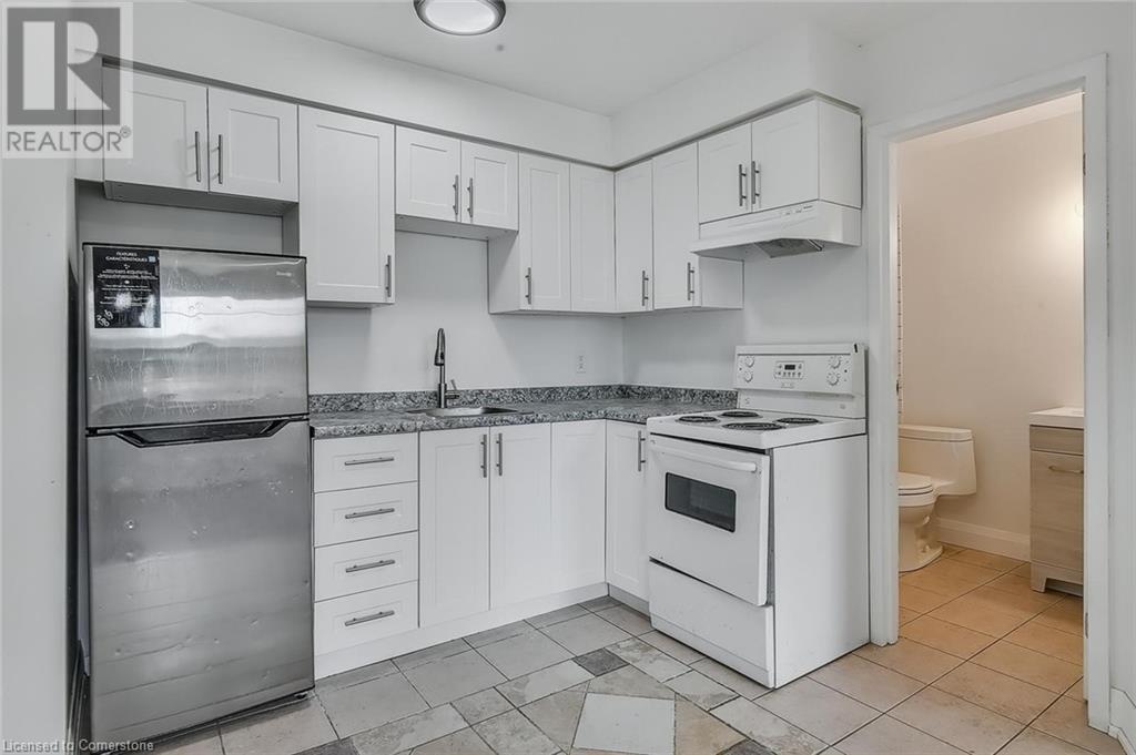 Kitchen with white electric stove, freestanding refrigerator, white cabinetry, under cabinet range hood, and light tile patterned floors - 897 Barton Street E, Hamilton, ON - Indoor Photo Showing Kitchen