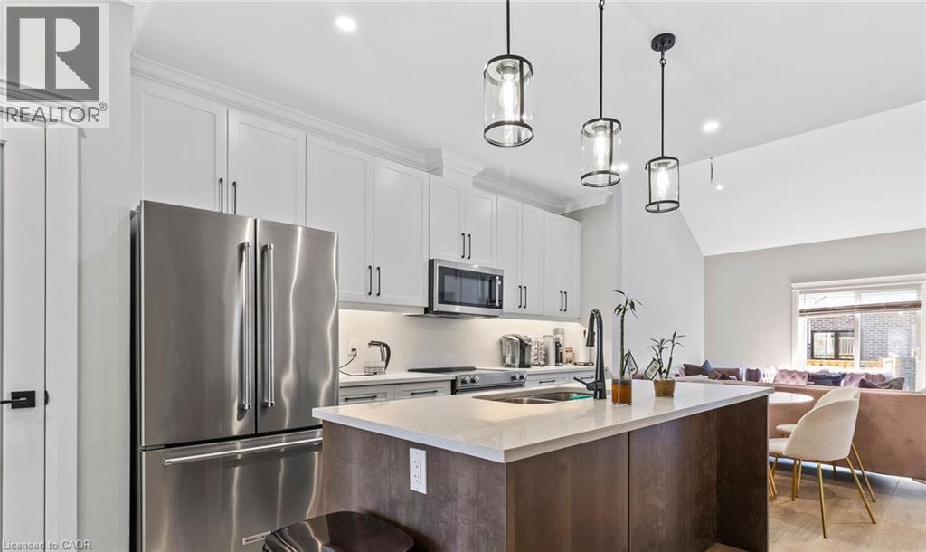 Kitchen with stainless steel appliances, open floor plan, an island with sink, light stone counters, and pendant lighting - 24 Tamarack Way, Simcoe, ON - Indoor Photo Showing Kitchen With Stainless Steel Kitchen With Double Sink With Upgraded Kitchen