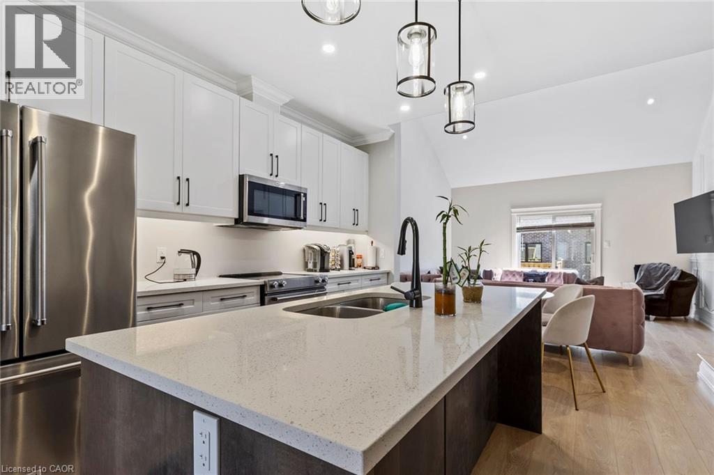 Kitchen with stainless steel appliances, pendant lighting, light stone countertops, open floor plan, and an island with sink - 24 Tamarack Way, Simcoe, ON - Indoor Photo Showing Kitchen With Stainless Steel Kitchen With Double Sink With Upgraded Kitchen