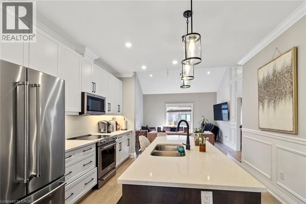 Kitchen featuring stainless steel appliances, light stone counters, open floor plan, decorative light fixtures, and a kitchen island with sink - 24 Tamarack Way, Simcoe, ON - Indoor Photo Showing Kitchen With Stainless Steel Kitchen With Double Sink With Upgraded Kitchen