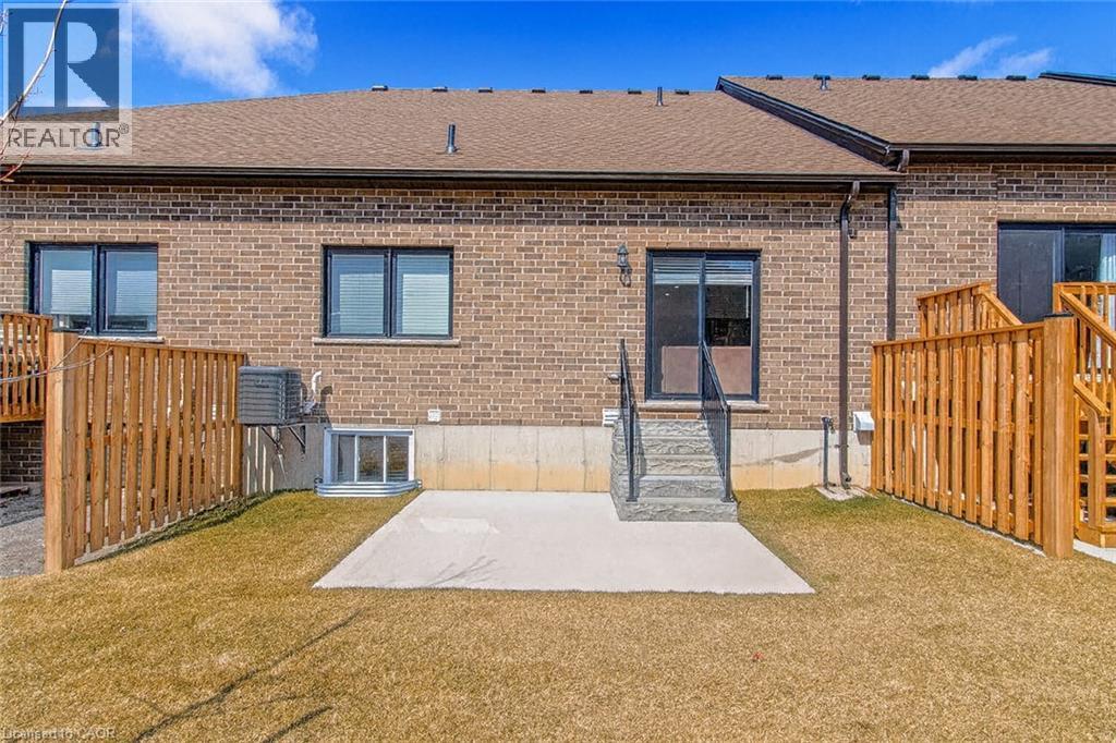 Rear view of house featuring roof with shingles, a patio area, brick siding, a lawn, and entry steps - 24 Tamarack Way, Simcoe, ON - Outdoor With Exterior