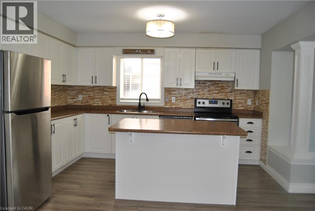 Kitchen featuring appliances with stainless steel finishes, dark countertops, white cabinets, under cabinet range hood, and backsplash - 154 Harding Street, Kitchener, ON - Indoor Photo Showing Kitchen With Double Sink