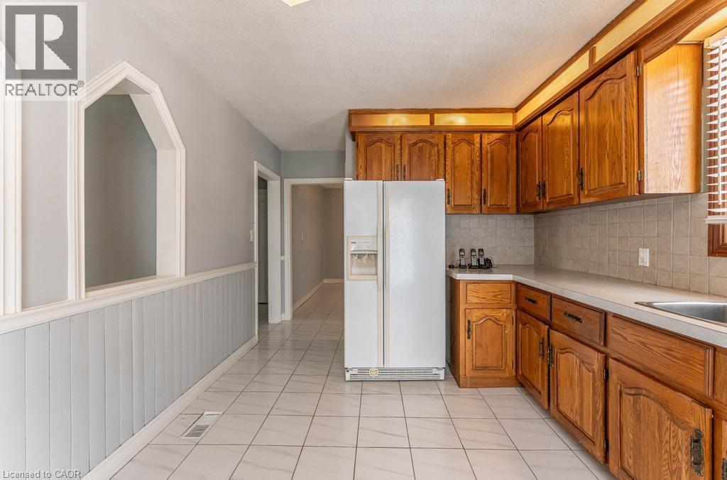 Kitchen with brown cabinetry, tasteful backsplash, white refrigerator with ice dispenser, and light countertops - 854 West 5Th Street, Hamilton, ON - Indoor Photo Showing Kitchen