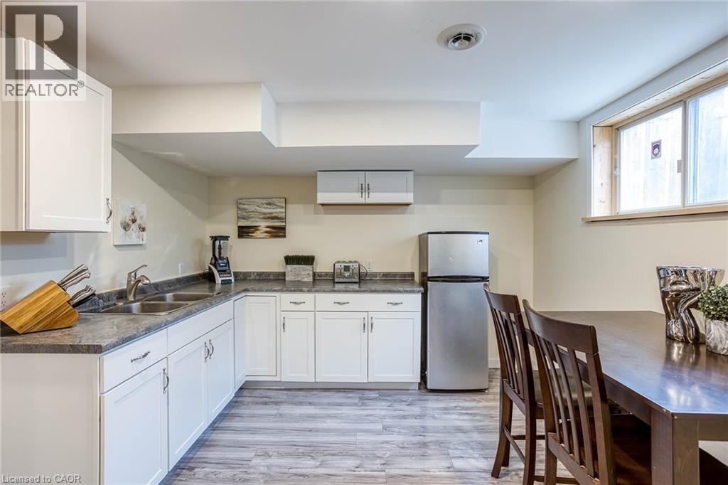 Kitchen featuring white cabinetry, freestanding refrigerator, light wood-style floors, and dark countertops - 310 Magnolia Drive, Hamilton, ON - Indoor Photo Showing Kitchen With Double Sink