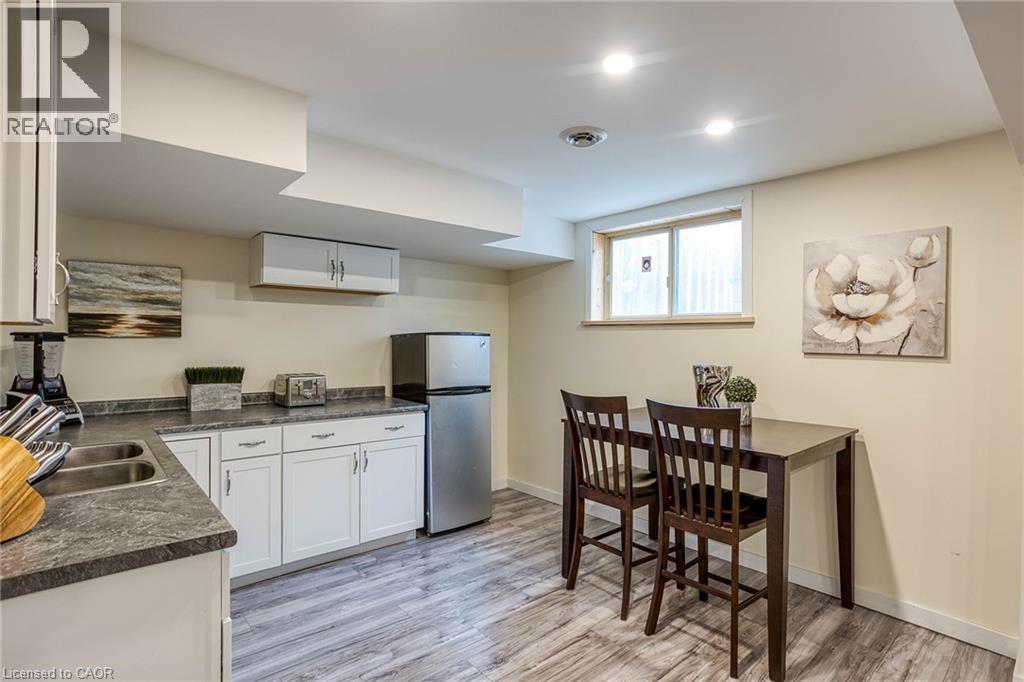 Kitchen with dark countertops, white cabinets, freestanding refrigerator, and light wood-style floors - 310 Magnolia Drive, Hamilton, ON - Indoor Photo Showing Kitchen With Double Sink