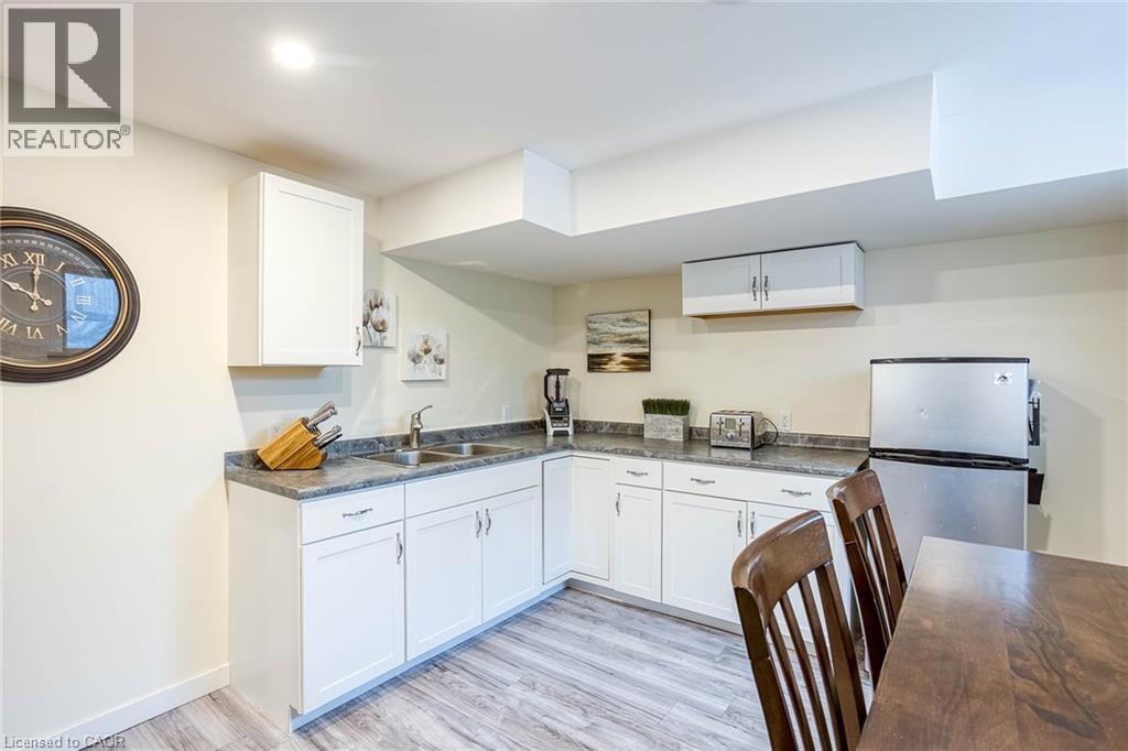 Kitchen with dark countertops, light wood-style flooring, white cabinetry, and freestanding refrigerator - 310 Magnolia Drive, Hamilton, ON - Indoor Photo Showing Kitchen With Double Sink