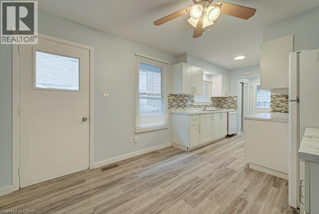 Kitchen with light countertops, white cabinetry, ceiling fan, light wood finished floors, and white appliances - 310 Magnolia Drive, Hamilton, ON