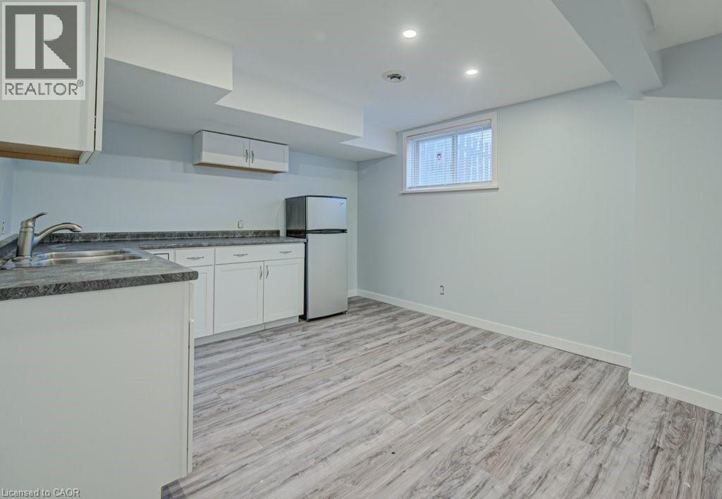 Kitchen with dark countertops, white cabinetry, freestanding refrigerator, light wood-style flooring, and recessed lighting - 310 Magnolia Drive, Hamilton, ON