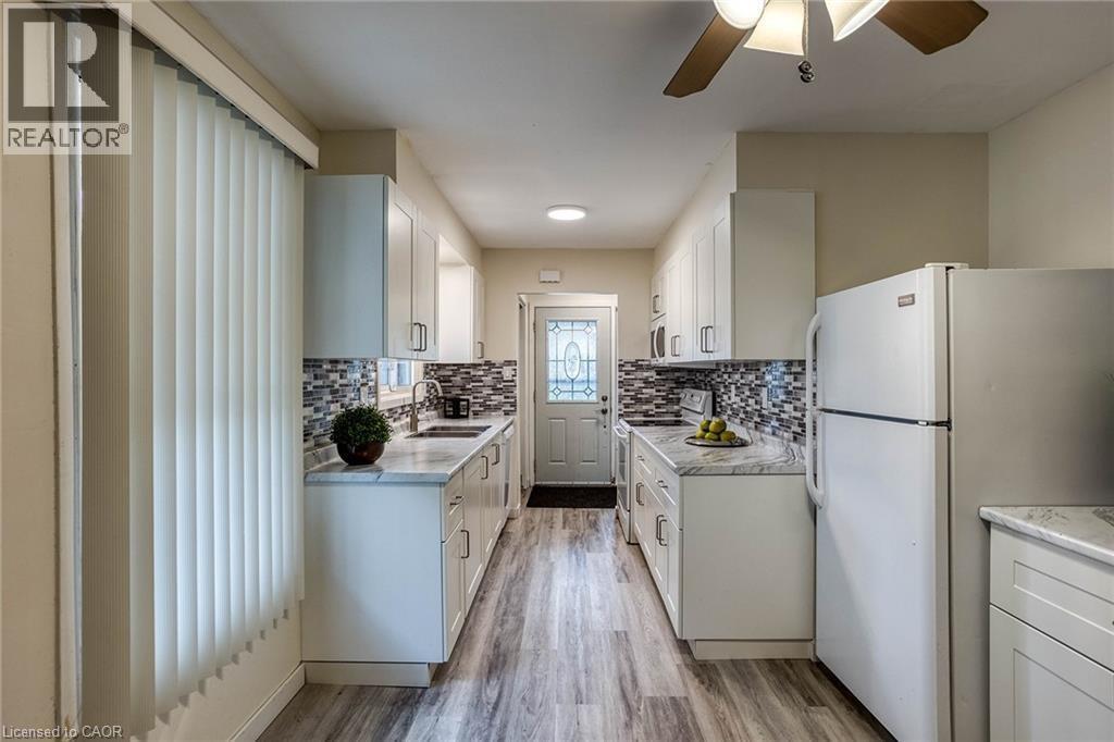 Kitchen with ceiling fan, white cabinets, white appliances, light wood-style flooring, and decorative backsplash - 310 Magnolia Drive, Hamilton, ON - Indoor Photo Showing Kitchen