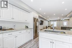 Kitchen featuring open floor plan, light stone counters, freestanding refrigerator, white cabinetry, and light wood-type flooring -