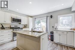 Kitchen with stainless steel appliances, white cabinetry, light wood finished floors, light stone counters, and a kitchen island with sink -