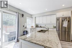 Kitchen featuring freestanding refrigerator, white cabinetry, light stone countertops, a kitchen island with sink, and light wood-style flooring -
