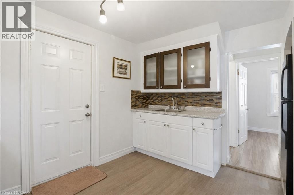 Kitchen with white cabinetry, freestanding refrigerator, glass insert cabinets, light wood finished floors, and backsplash - 260 Prospect Street S, Hamilton, ON - Indoor Photo Showing Other Room
