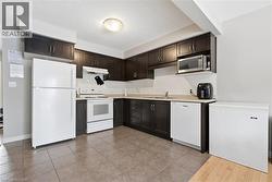 Kitchen with white appliances, light countertops, dark brown cabinets, under cabinet range hood, and backsplash -