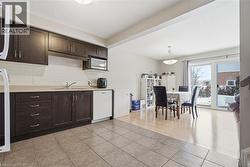 Kitchen featuring dark brown cabinetry, light countertops, light tile patterned floors, and white appliances -
