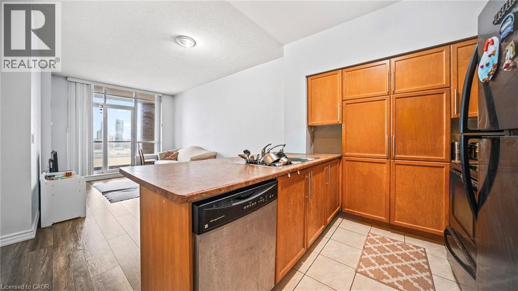 Kitchen with brown cabinetry, black appliances, expansive windows, a textured ceiling, and a peninsula - 388 Prince Of Wales Drive Unit# 1609, Mississauga, ON - Indoor Photo Showing Kitchen With Double Sink