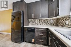 Kitchen with black appliances, dark wood finish cabinets, light countertops, and backsplash -