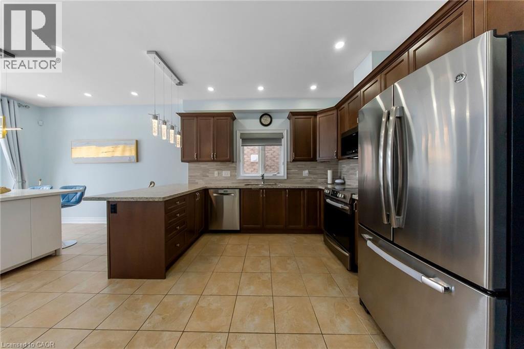 Kitchen featuring stainless steel appliances, a peninsula, dark wood finish cabinetry, pendant lighting, and light tile patterned flooring - 59 Greti Drive, Hamilton, ON - Indoor Photo Showing Kitchen