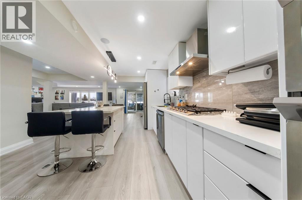 Kitchen with modern cabinets, white cabinetry, a breakfast bar, light wood-style floors, and a kitchen island with sink - 59 Greti Drive, Hamilton, ON - Indoor Photo Showing Kitchen With Upgraded Kitchen