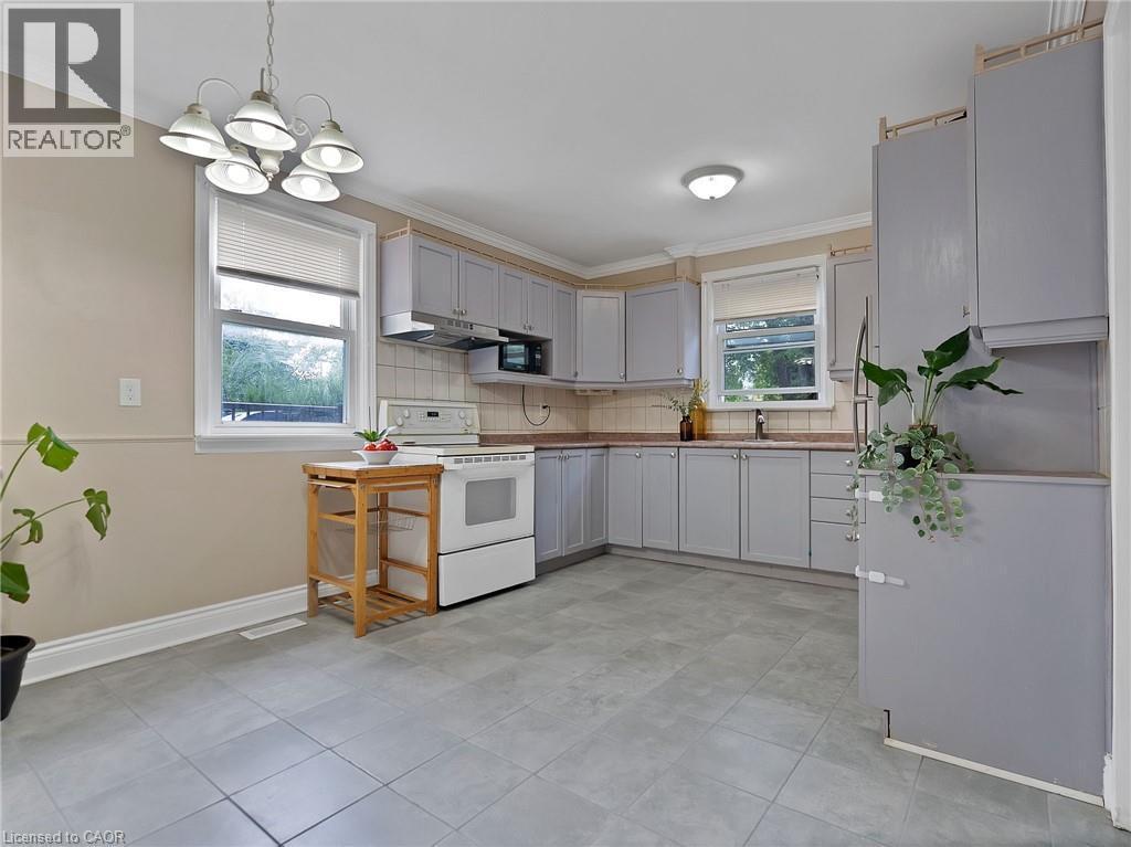Kitchen with white electric stove, decorative light fixtures, ornamental molding, backsplash, and gray cabinetry - 210 East 24Th Street, Hamilton, ON - Indoor Photo Showing Kitchen