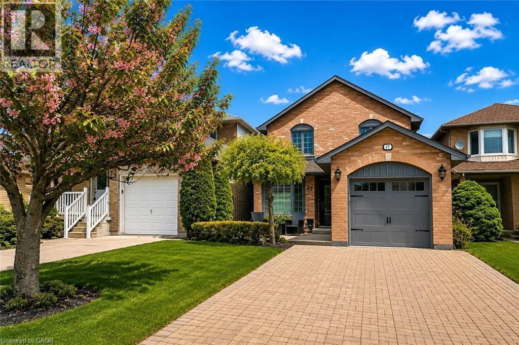 Brick exterior featuring a two-car garage with an arched stone facade, paver driveway, and manicured front lawn - 27 Beaverton Drive, Hamilton, ON - Outdoor With Facade