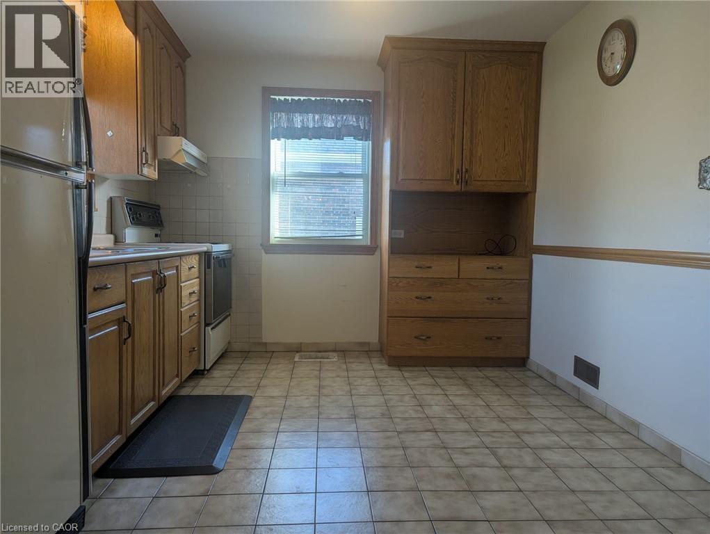 Kitchen with freestanding refrigerator, white electric range oven, brown cabinets, light countertops, and under cabinet range hood - 59 Dunkirk Drive, Hamilton, ON - Indoor Photo Showing Kitchen