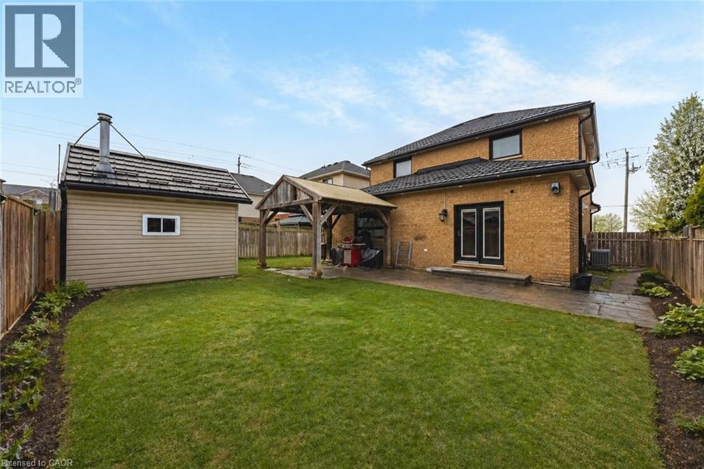Expansive rear yard featuring a large green lawn, a wooden storage shed with a shingled roof, a covered outdoor structure, a stone patio, and perimeter fencing - 6 Second Road W, Hamilton, ON - Outdoor